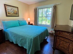 Bedroom with a queen sized bed, two night stands dresser and TV.